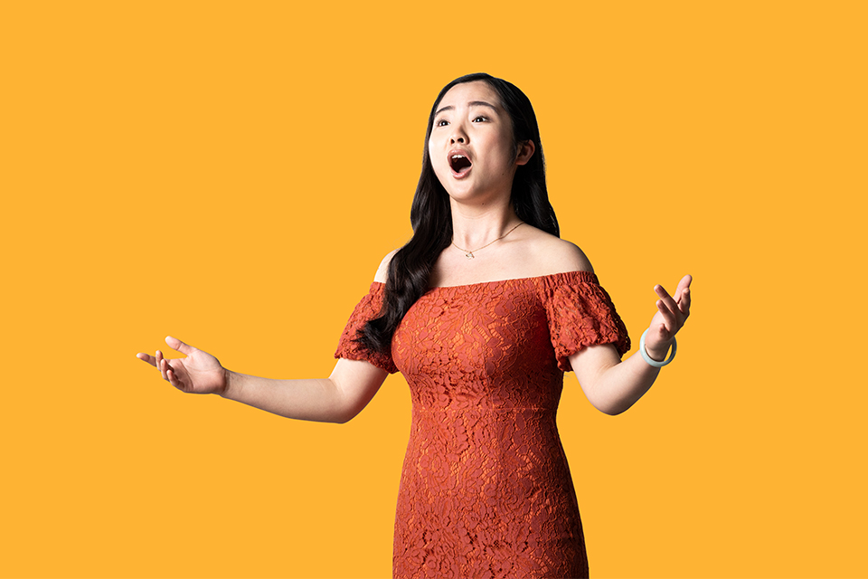A student singing in a red dress against a yellow background